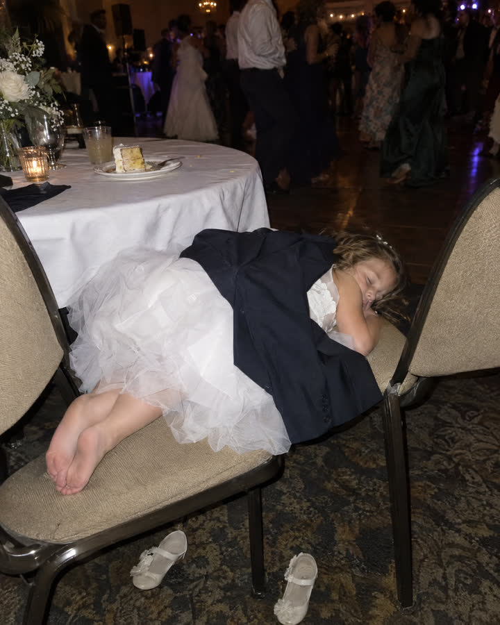 A flower girl asleep across two chairs late at night